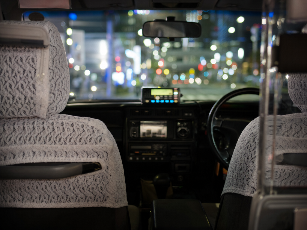 Pristine rear interior of a Japanese taxi with white lace seat covers, soft cabin light, blurred night city through windshield